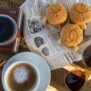 Coffee, cookies, camera, and sunglasses on a table.